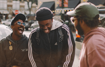 Three students talking and laughing outdoors. Jed Villejo on Unsplash.
