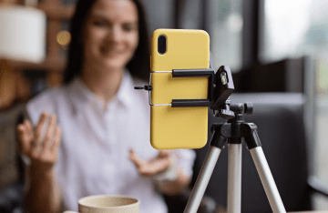 A young woman live streaming using a yellow smartphone on a tripod in a cafe