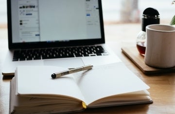 Open laptop and open notebook with pen on desk