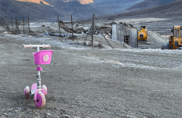 A pink scooter sits on an empty mountain trail near a landfill