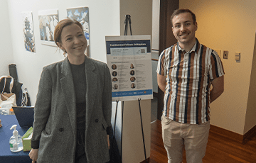 Two staff members posing with an even poster