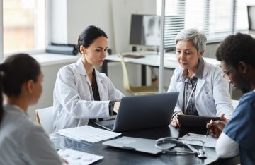 two doctors looking at a laptop next to two doctors sitting at a table