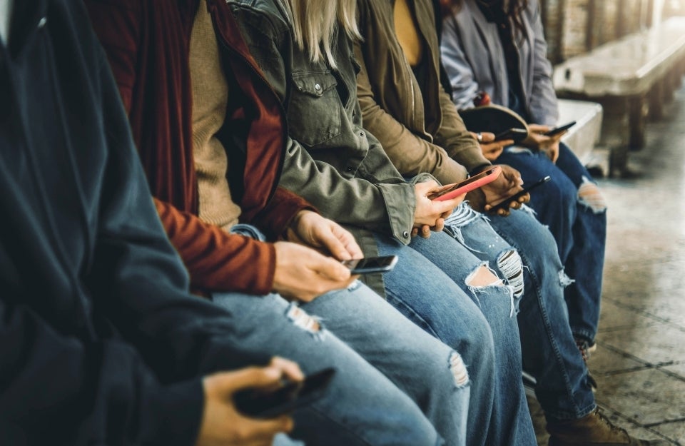 Five people sit on a bench looking at their smart phones