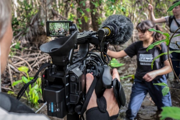 Students being filmed as they walk through a swamp