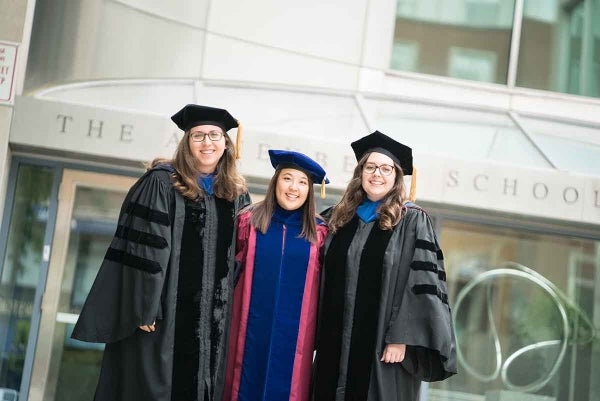 Three women in graduation regalia standing in front of the Annenberg building
