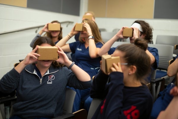 Group of female students looking into virtual reality goggles that are made of cardboard