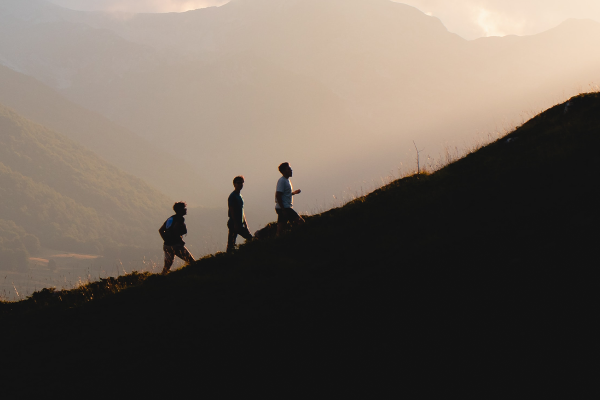 Silhouette of three people walking up a mountain