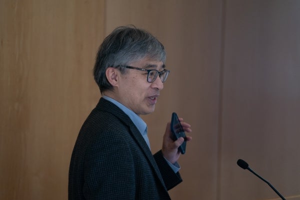 Professor Guobin Yang holding up a phone at a podium