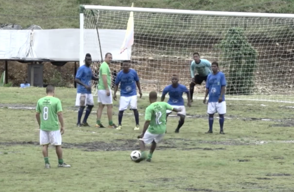 A soccer team playing on a field. A man is about to kick a ball into the goal net.