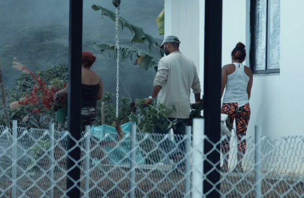 Three people standing outside of a white building with a fence in the foreground