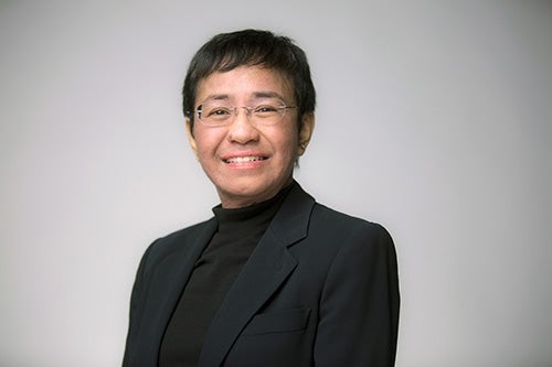 Maria Ressa in a black suit smiling against a white background