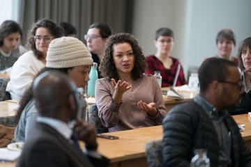 Woman speaking while seated amid many other people