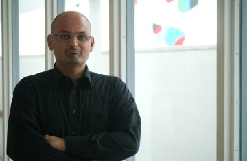 Marwan Kraidy poses in a black shirt with his arms folded in front of big glass windows.