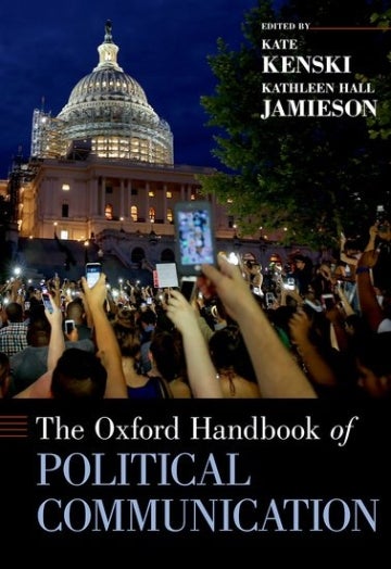 Cover of 'The Oxford Handbook of Political Communication', edited by Kathleen Hall Jamieson, Dan Kahan, and Dietram A. Scheufele. The cover is an image of a huge group of people standing in in front of a building. They all have their arms up with their phones in their hand. It is night-time in the picture, so the screens glow in the picture. At the bottom of the cover is the title and the top right has the editors' names. 