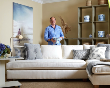 Joe Ruggiero standing behind a sofa holding a ceramic pot with various decor elements around him