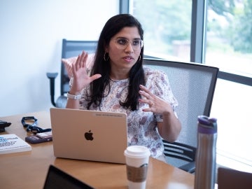 Madhavi Reddi sits at a table with a laptop talking to someone offscreen